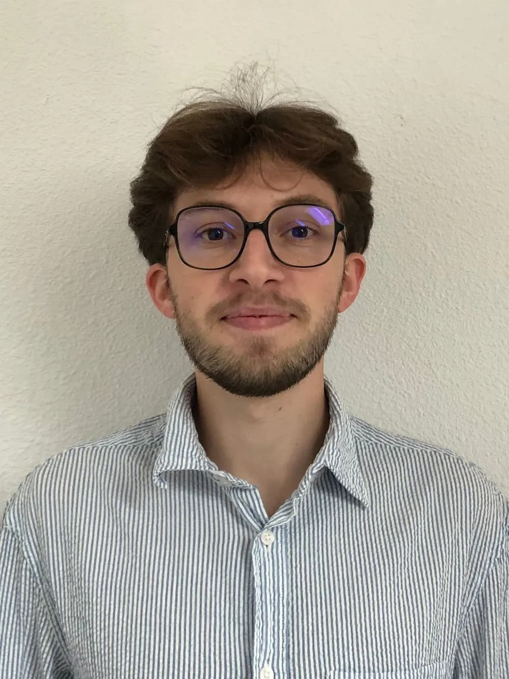 Portrait d'Axel Blanchard, en chemise rayée, devant un mur clair