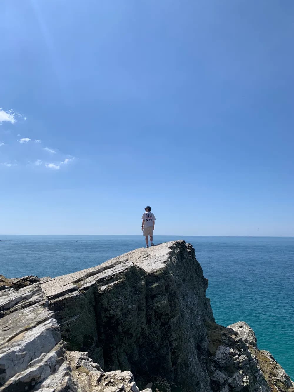 Axel Blanchard, de dos, debout sur un rocher face à la mer